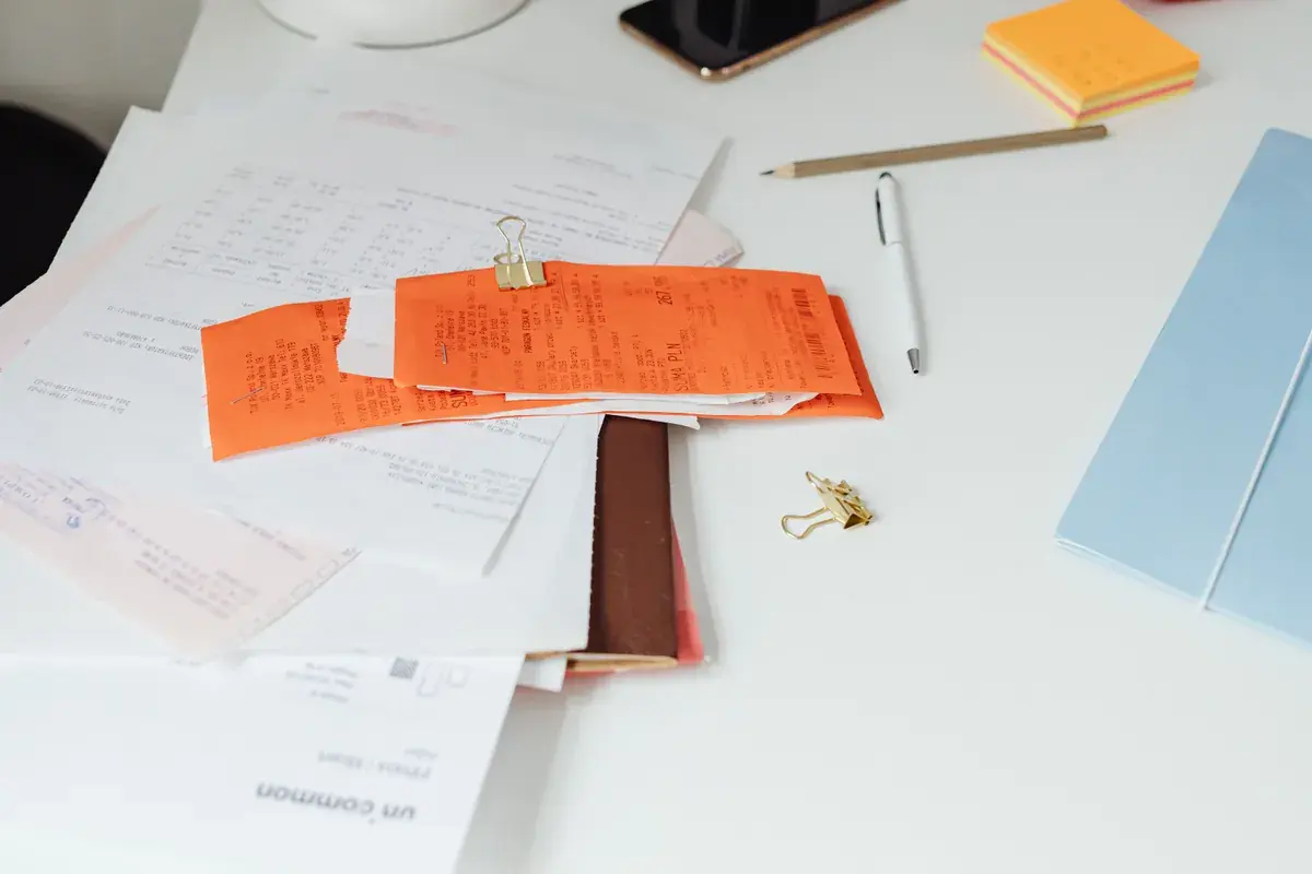 A tidy white desk with paper receipts, printed statements, a pen and clips arranged in neat stacks.