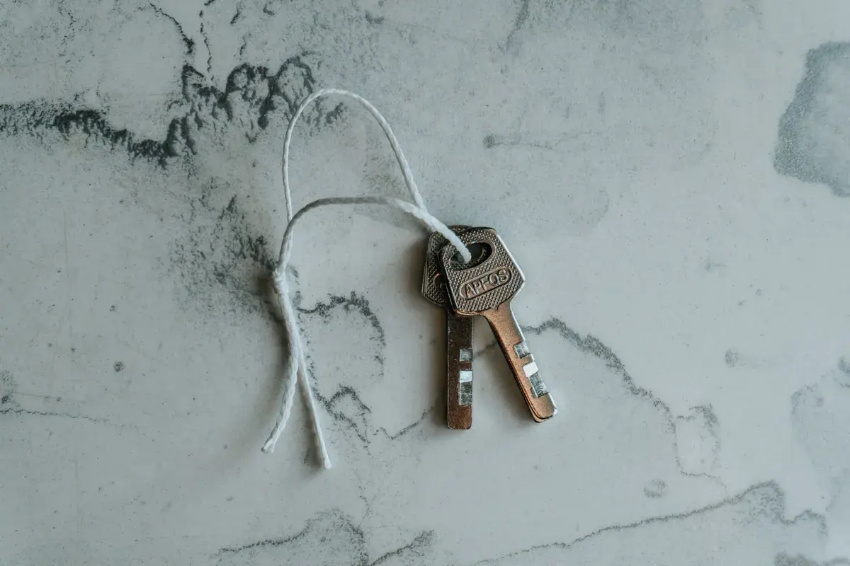 Two metal house keys on a string resting against a soft marbled background