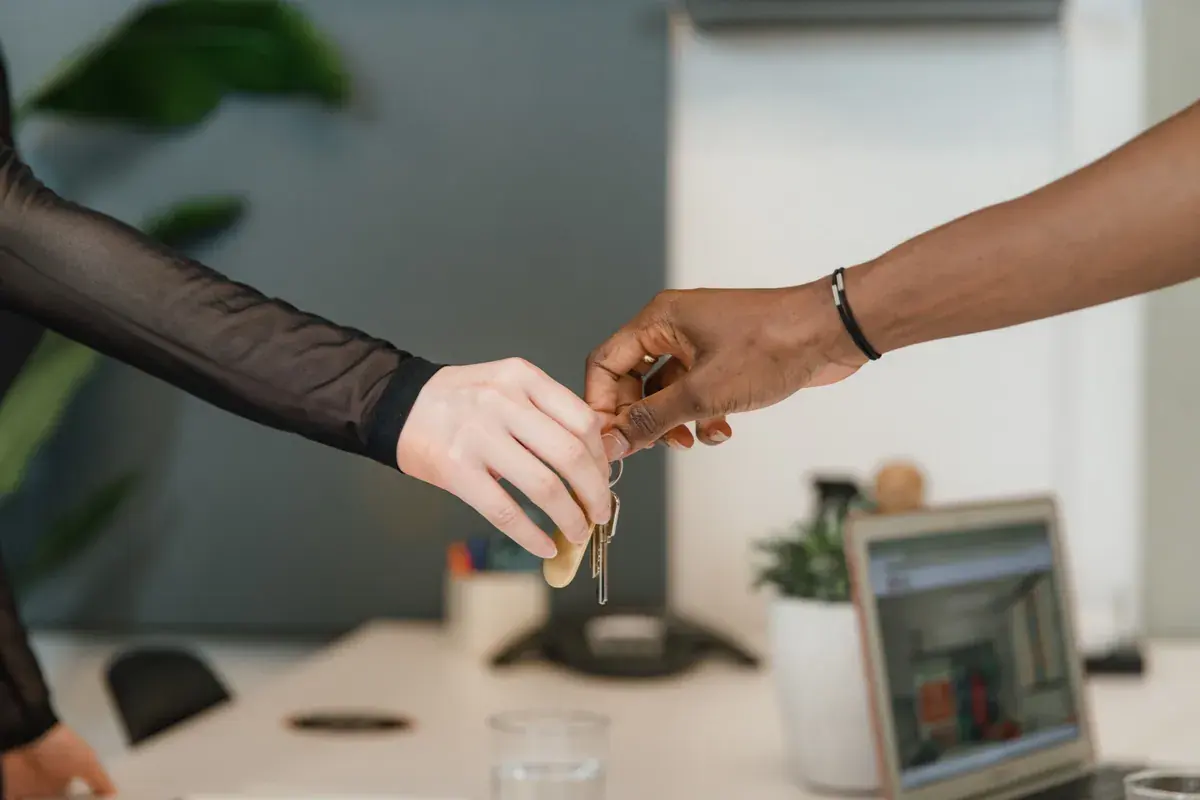 A pair of house keys and a folded contract passed across a professional office desk
