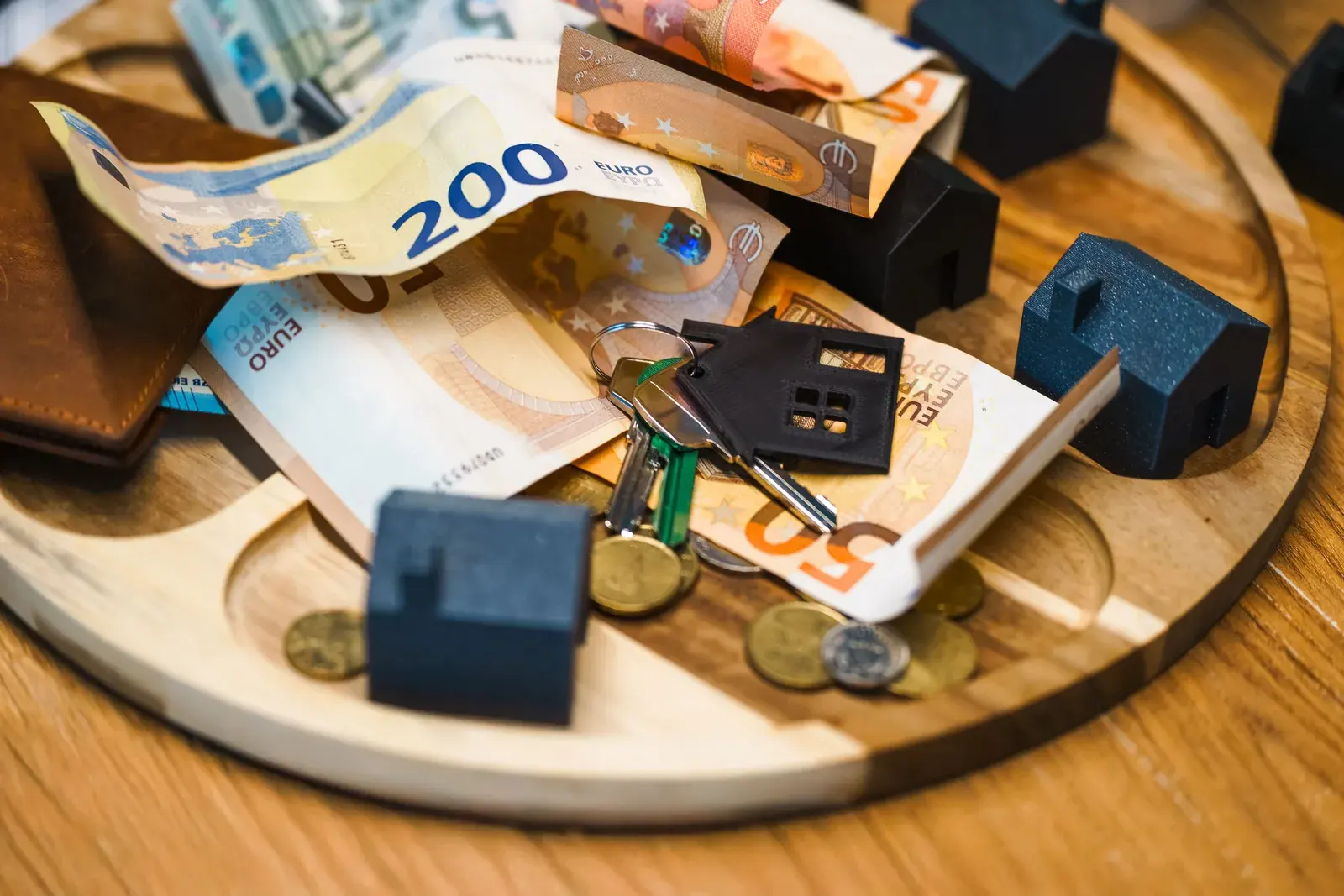 House keys resting alongside miniature model houses and paper currency on a bright surface