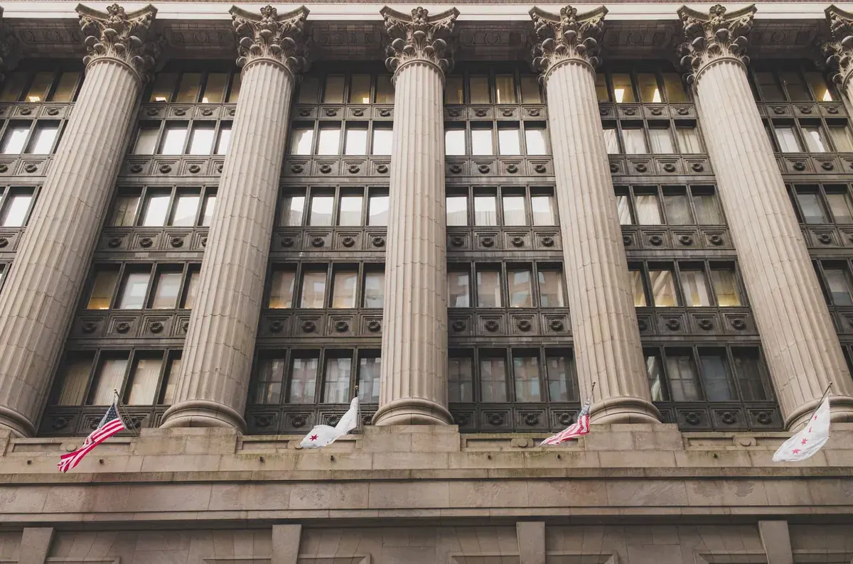 A downtown facade of tall stone columns with American flags hanging across the lower stories