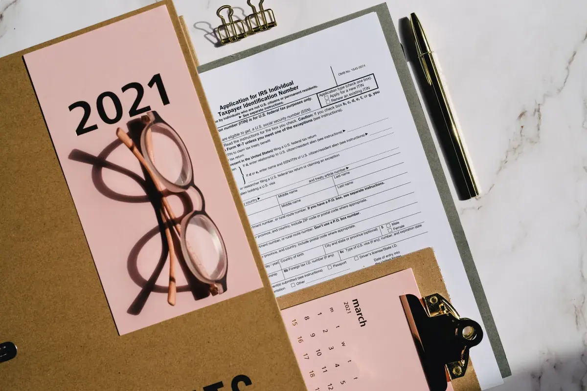 Flat lay of printed federal tax forms, a calendar, and reading glasses on a wooden surface