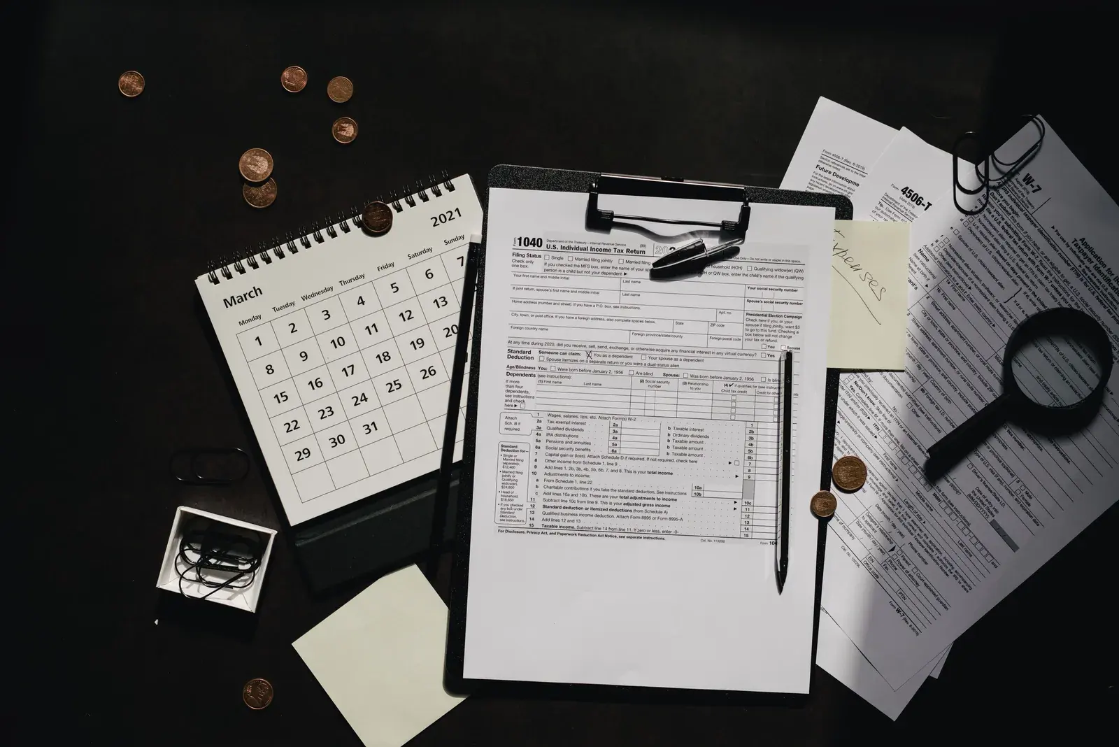 A neatly organized workspace with printed federal tax forms, a calendar, and a magnifying glass