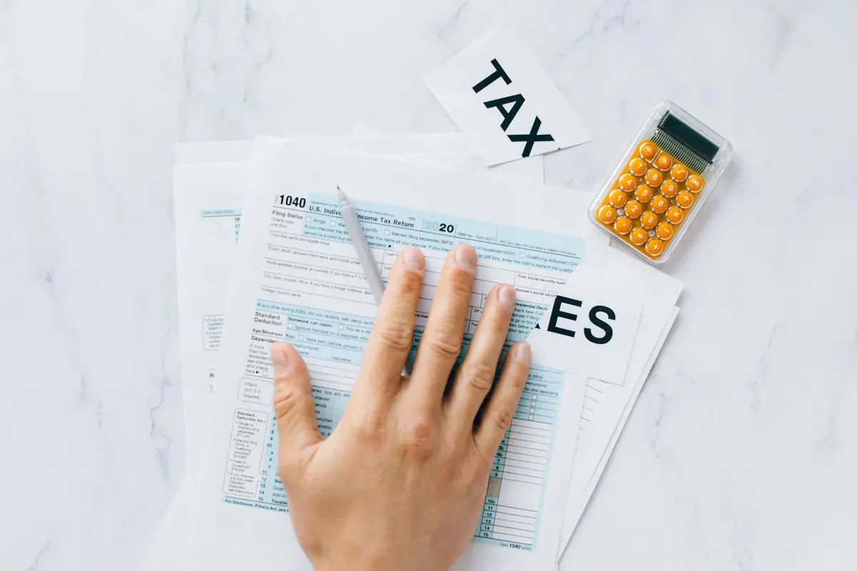 Overhead view of a hand resting on a printed federal income tax return beside a calculator