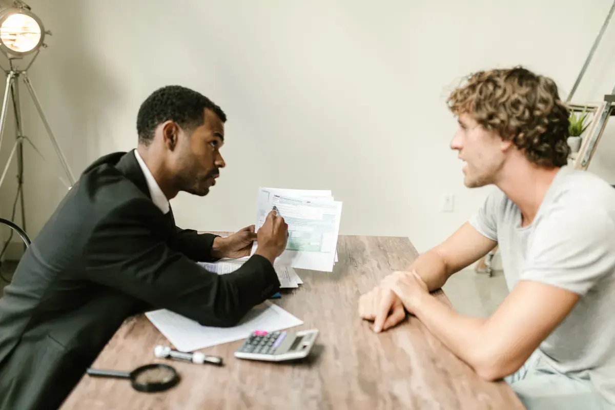 Two people at a desk reviewing printed tax forms, with a calculator and a magnifying glass nearby