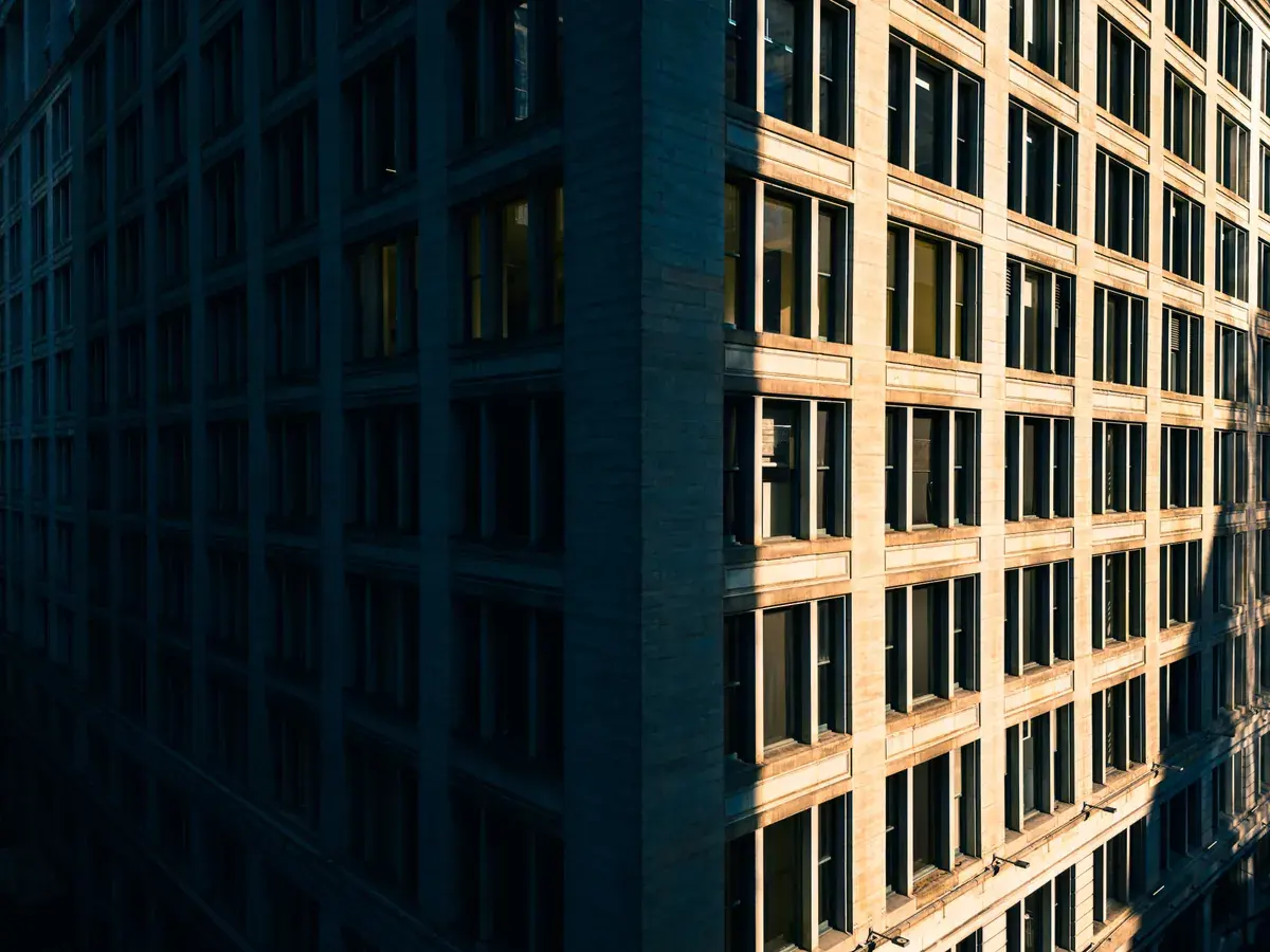 A dramatic view of an urban building corner at sunset with deep shadows across its facade