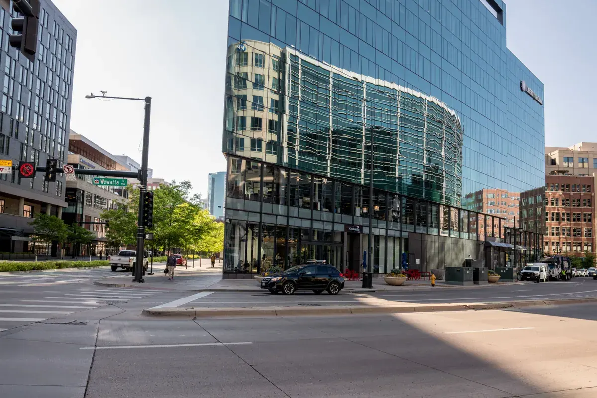 A quiet downtown intersection with a modern glass-fronted office building and a parked car