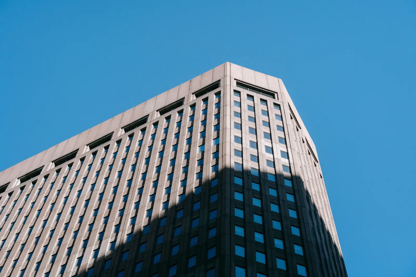 A tall limestone high-rise building rising against a blue sky, viewed from the street