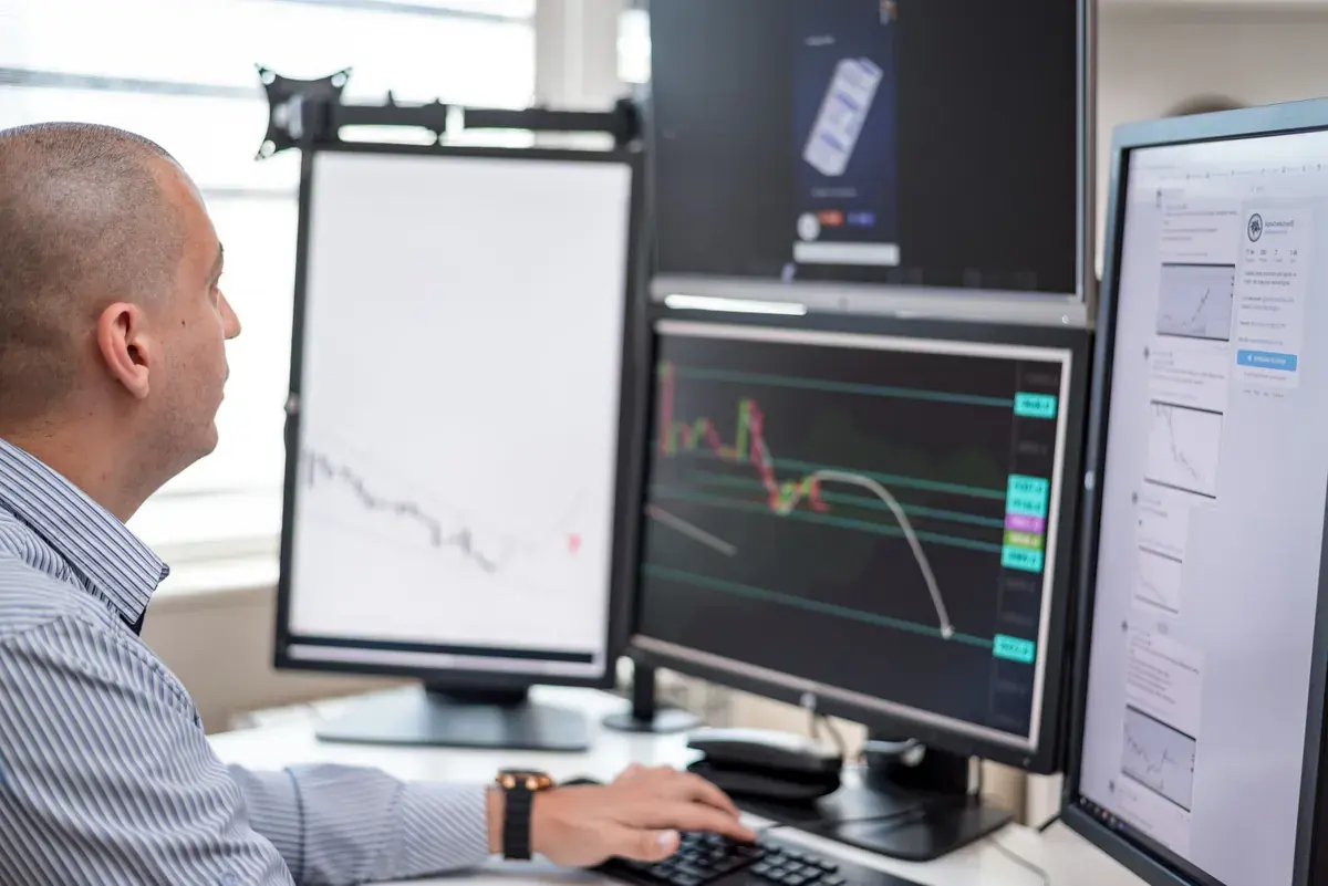 A person in a striped shirt studies market charts across a bank of desktop monitors