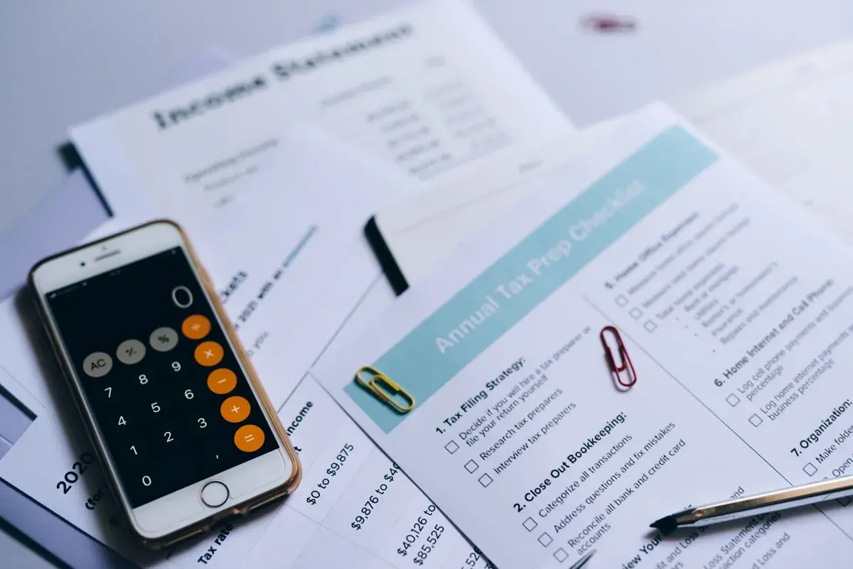 Lista impresa de preparación de impuestos y un estado de resultados en un escritorio junto a un teléfono con calculadora