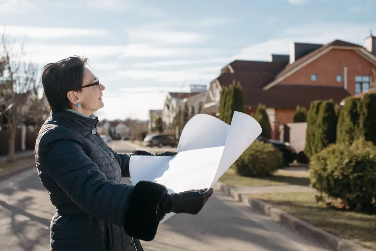 Person holding a large plan sheet on a residential street lined with houses