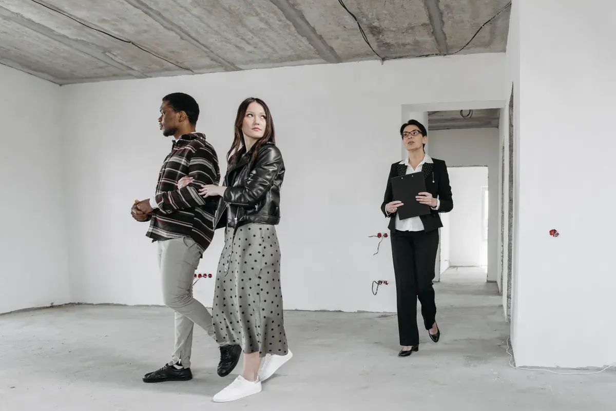 Three people walking through a bare unfinished apartment, one carrying a clipboard