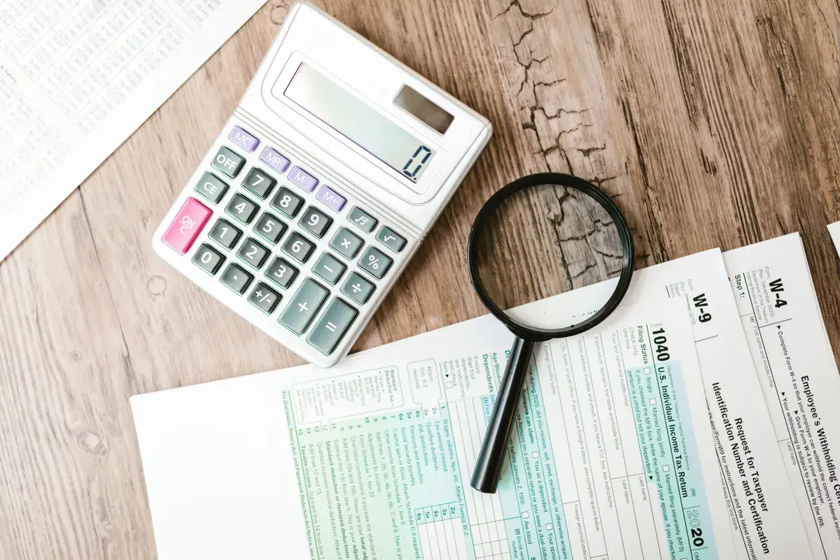 A magnifying glass and calculator resting over IRS Form 1040, W-9, and W-4 documents.