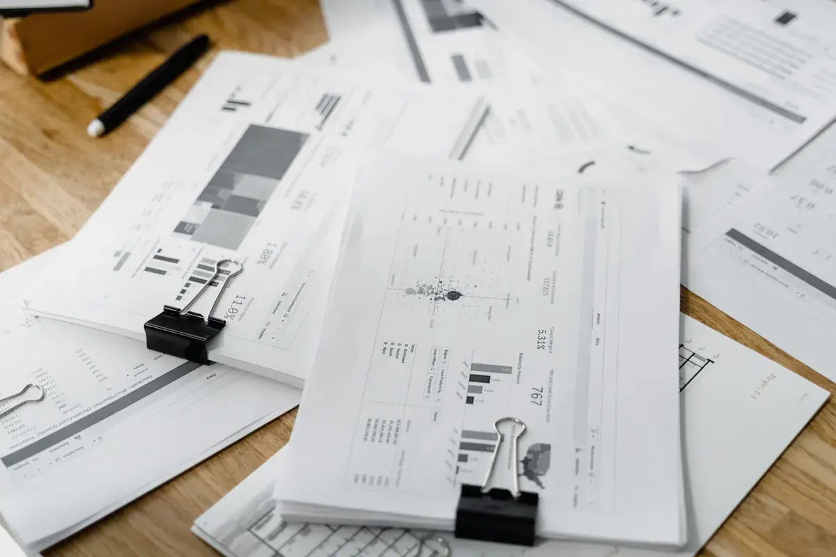 Stacks of printed financial reports and charts held with binder clips, spread across a wooden desk.