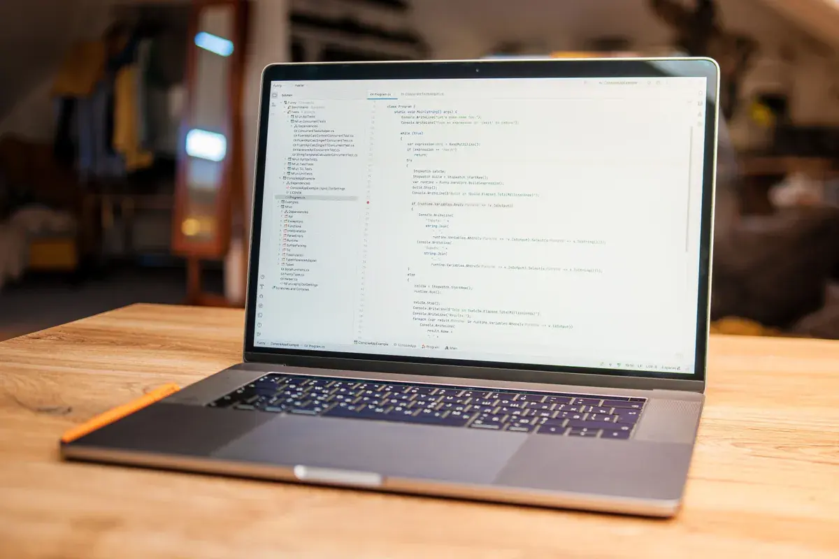 An open laptop shows lines of code on screen on a wooden desk in a modern workspace