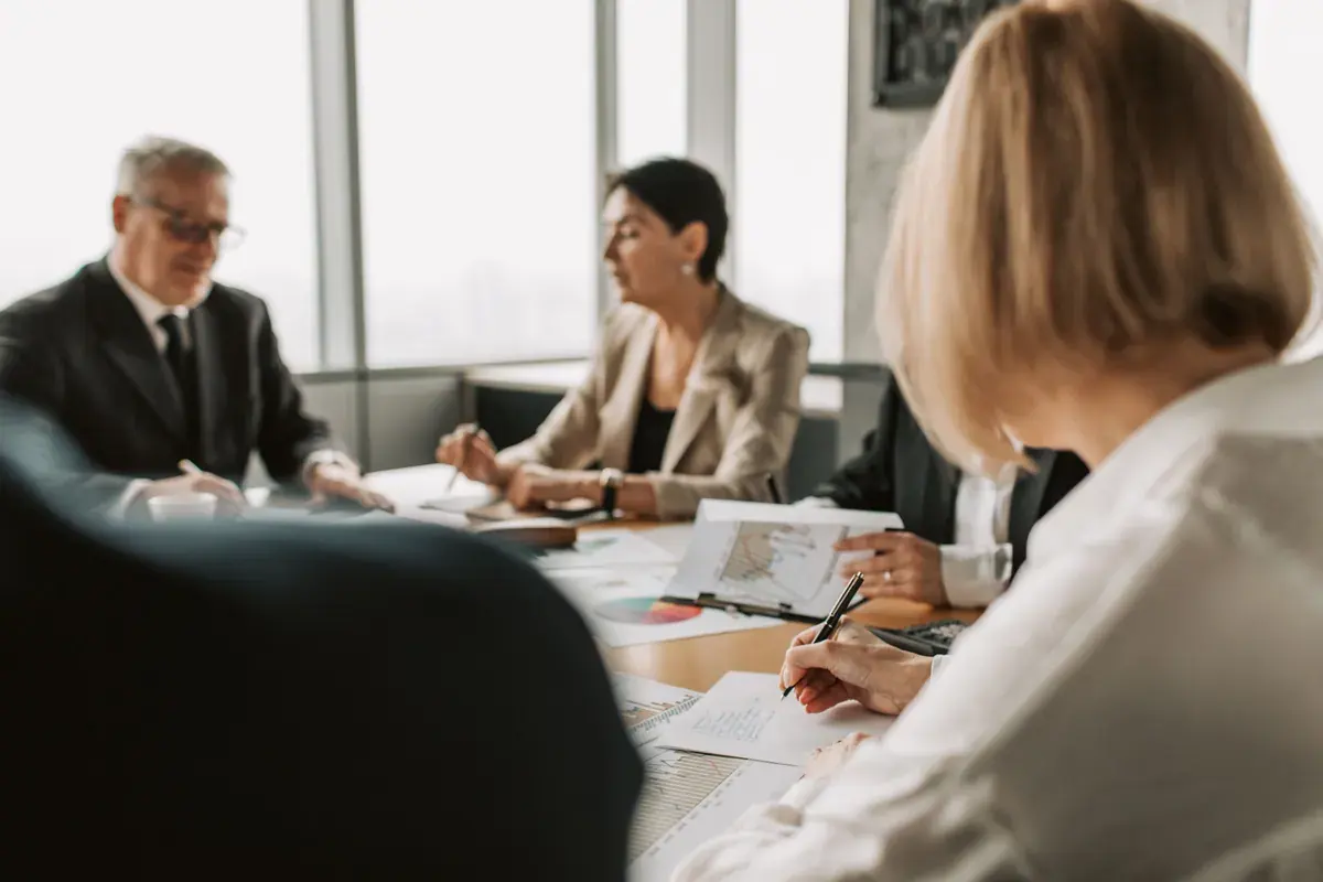 Colleagues seated around a conference table reviewing printed charts and documents in a bright office