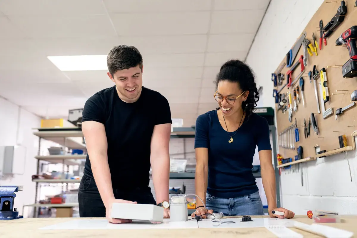 Two people testing a prototype device on a workbench in a tool lined workshop