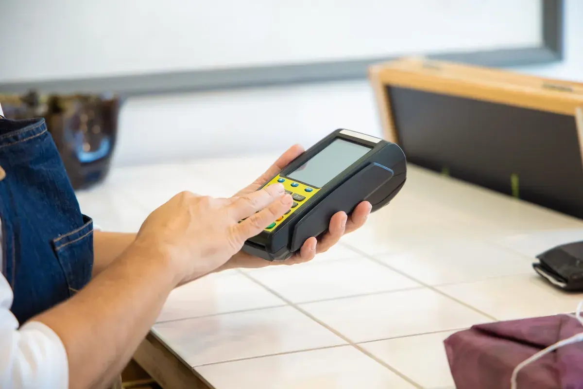 Hands entering an amount on a handheld card payment terminal at a counter