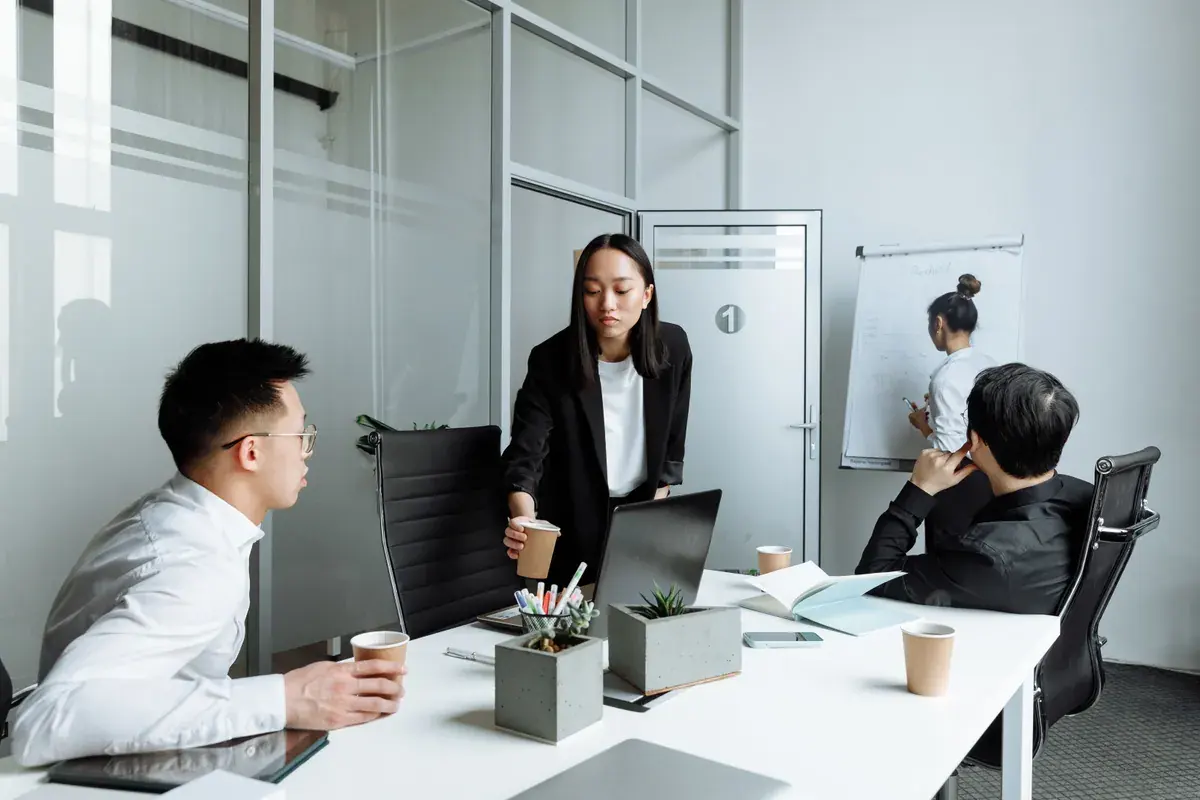 An office team gathered around a conference table discussing a project binder in a bright meeting room