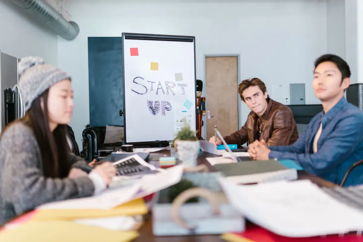 Un pequeño equipo de startup sentado alrededor de una mesa desordenada con laptops y una pizarra detrás