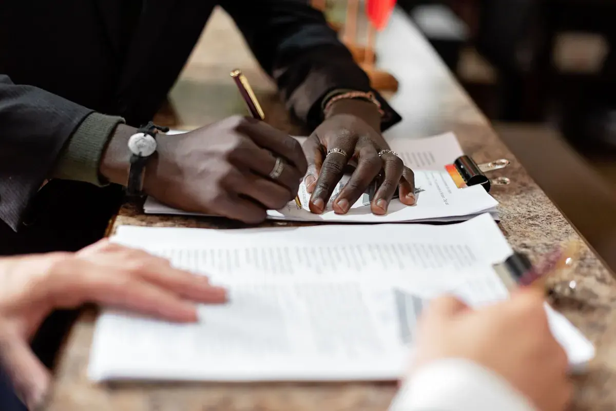 Close view of several pairs of hands signing and reviewing printed documents at a counter