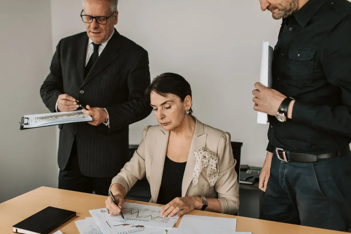 Three colleagues in an office reviewing printed charts spread across a desk