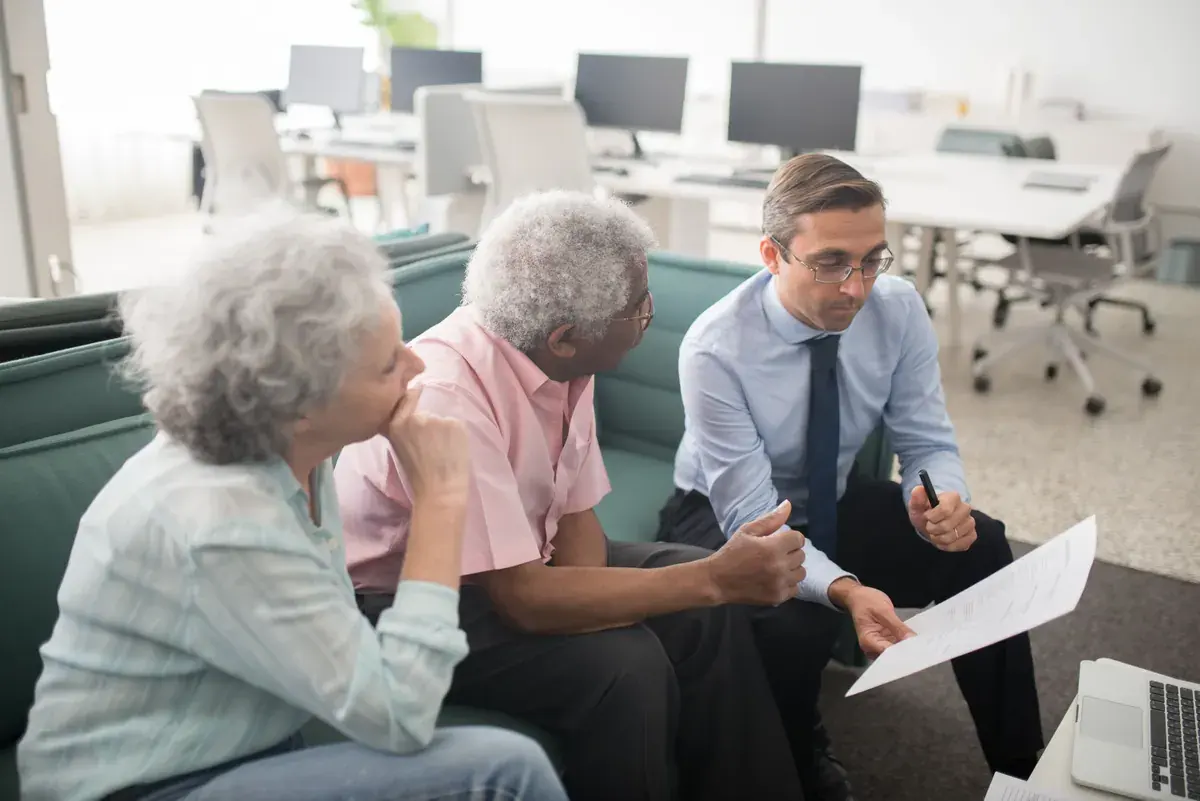 A professional consulting two older clients across a desk with paperwork visible