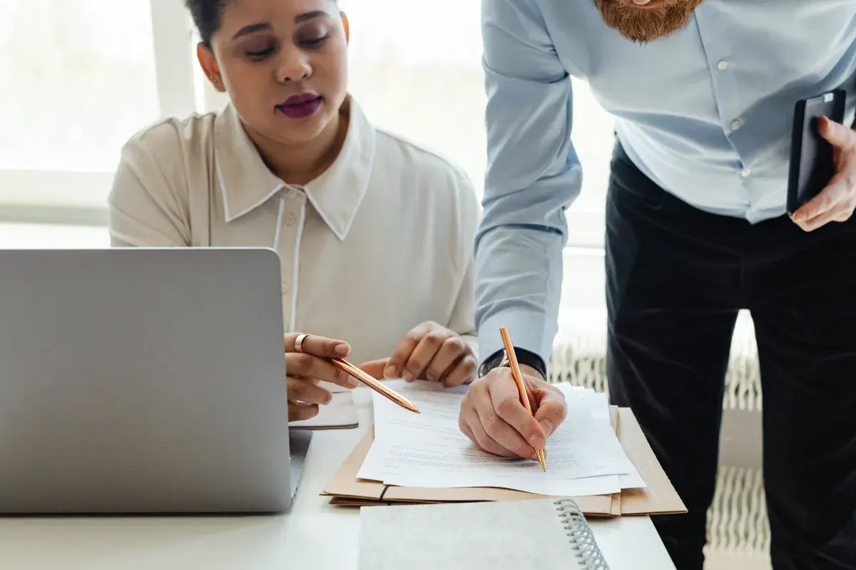 Two colleagues collaborate on paperwork during an office meeting at a wooden table