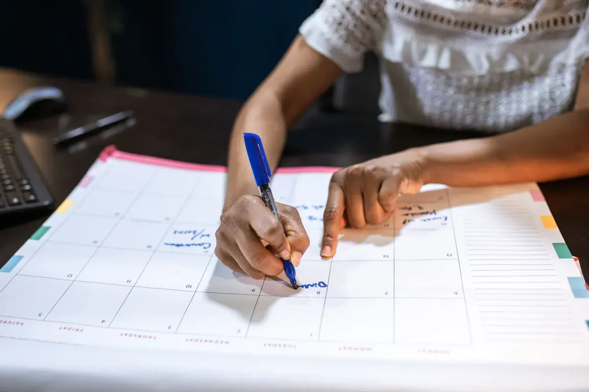 Manos marcando fechas en un calendario de escritorio de papel junto a un teclado