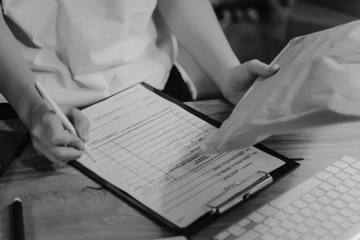 Black-and-white photo of a person taking notes on a clipboard beside a keyboard