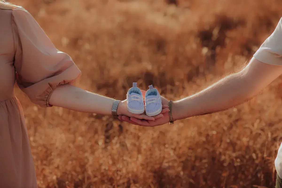 Dos padres sostienen un par de zapatitos de bebé en sus manos en un campo iluminado por el sol
