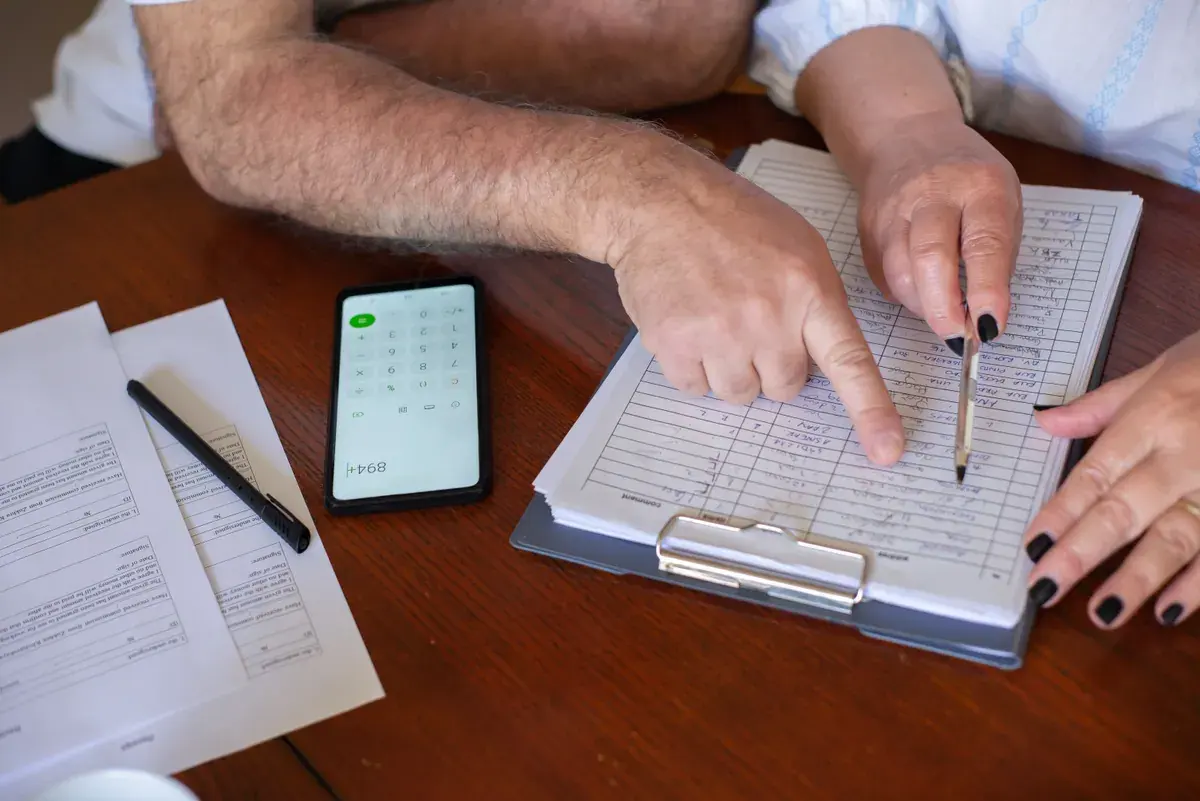 Two people at a wooden table going over a checklist together, with a pen and a phone calculator nearby