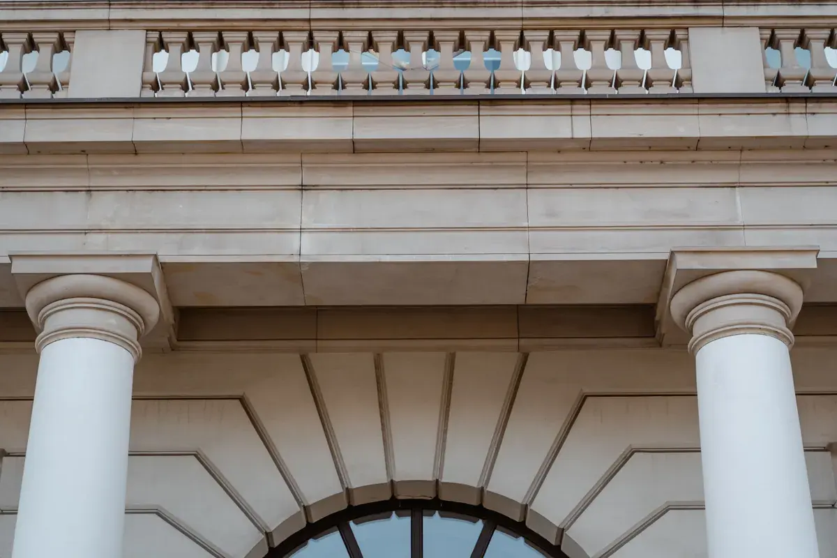 Low angle view of pale stone columns and a carved arch on a classical building facade.